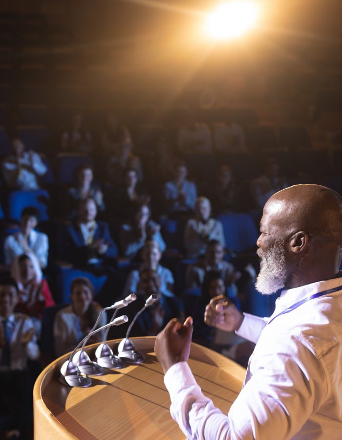 Businessman standing near podium and giving speech to the audience in the auditorium